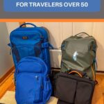 Four carry-on travel bags lined up by the door — a blue roller bag, blue daypack, green roll-top backpack, and black laptop bag — the ultimate carry-on packing system for travelers over 50 from TravelPast50.com.
