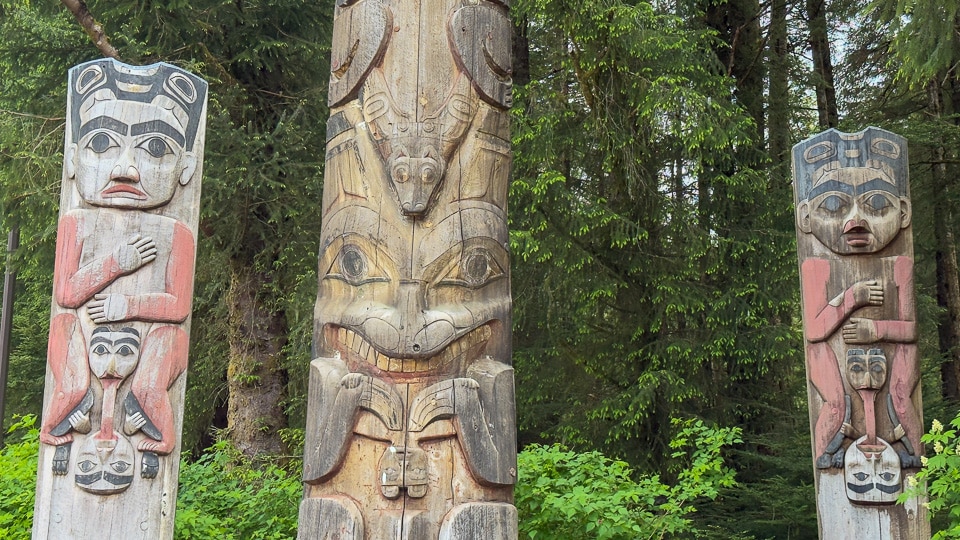 Three totem poles standing together in the coastal rainforest at Sitka National Historical Park, Alaska