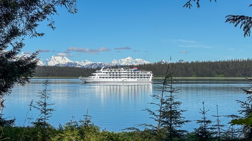 American Cruise Lines' American Constitution sailing through calm waters near Bartlett Cove, Alaska, with forested shoreline in the background