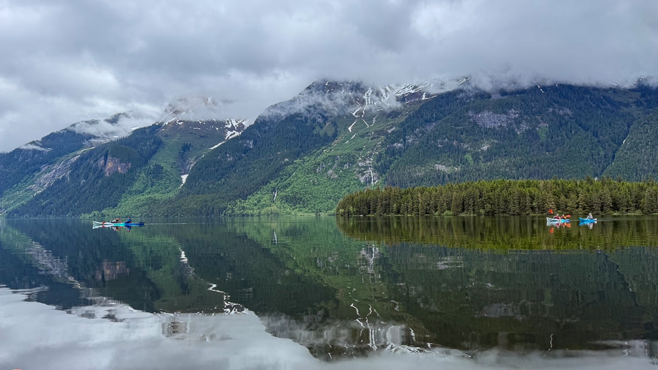 Small kayaking group paddling on Chilkoot Lake near Haines, Alaska, surrounded by forested mountains