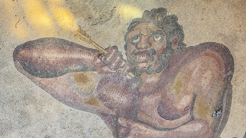 Close-up of a bearded giant grimacing as he pulls an arrow from his shoulder, mosaic at the Villa Romana del Casale