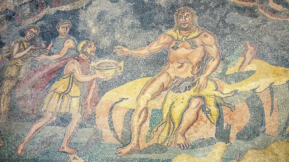Ulysses offering a bowl of wine to the seated giant Polyphemus as his companions pour more, mosaic at the Villa Romana del Casale