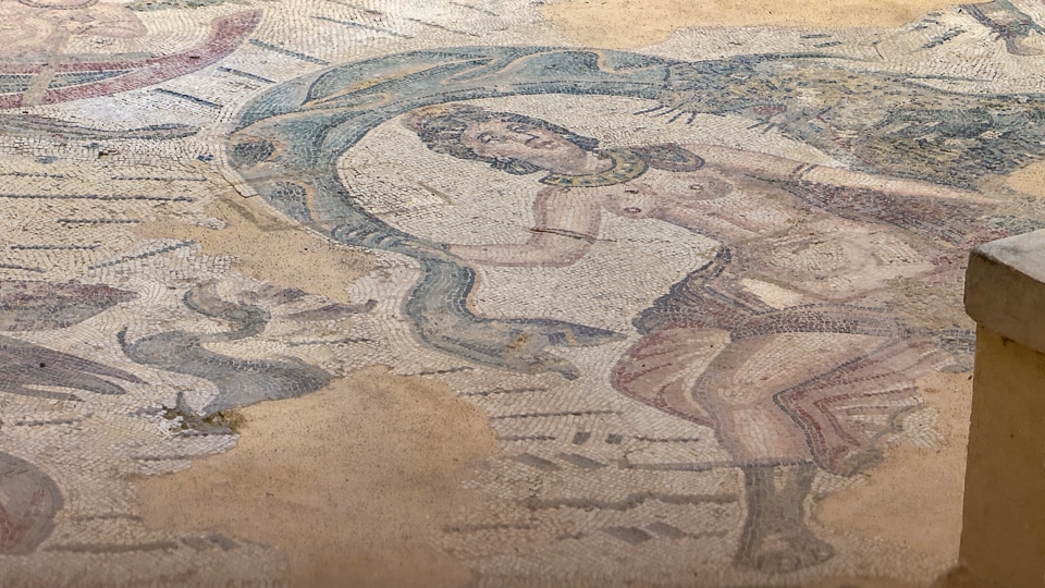 Faded mosaic of a Nereid seated on a scaly sea monster whose blue-green tail arcs over her head, in the frigidarium of the Villa Romana del Casale
