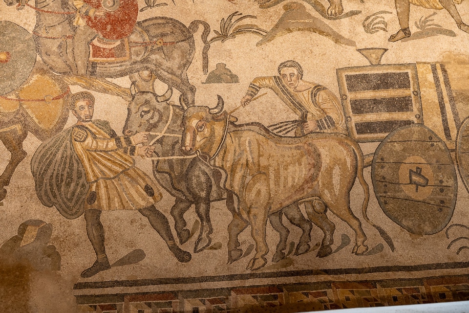 Two oxen pulling a cart loaded with a wooden animal crate, led by one man and driven by another, Great Hunt mosaic