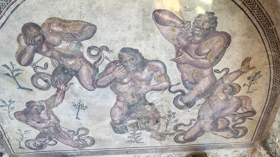Five giants with serpent-tailed legs writhing in pain in a semicircular apse mosaic at the Villa Romana del Casale